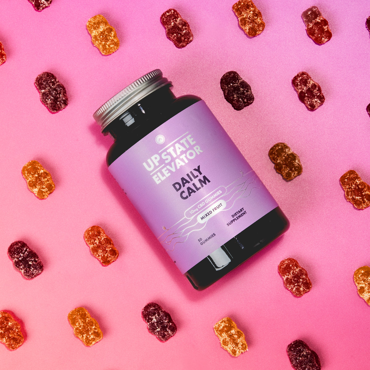 Upstate Elevator Daily Calm CBD gummies bottle with assorted mixed fruit CBD gummies on pink background