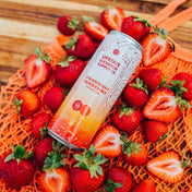 Upstate Elevator strawberry tangerine THC seltzer can surrounded by fresh strawberries on an orange net bag